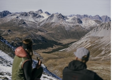 2 Personen sitzen vor Bergpanorama